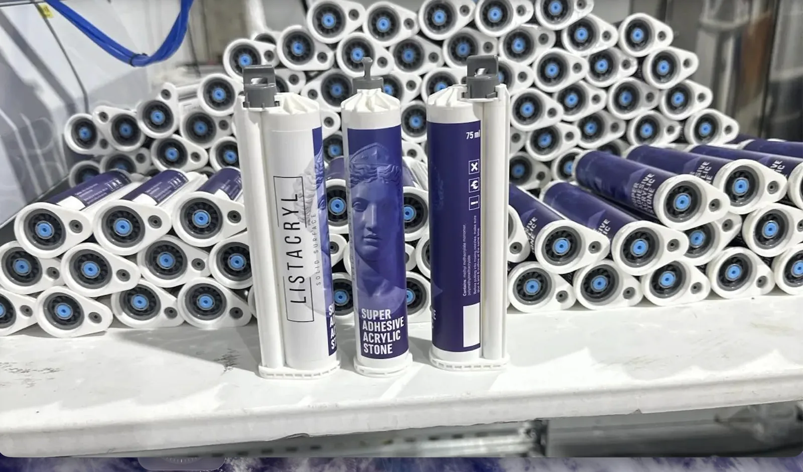 Картриджи клея LISTACRYL Super Adhesive Acrylic Stone на участке фасовки: три картриджа стоят на столе перед штабелем готовой партии